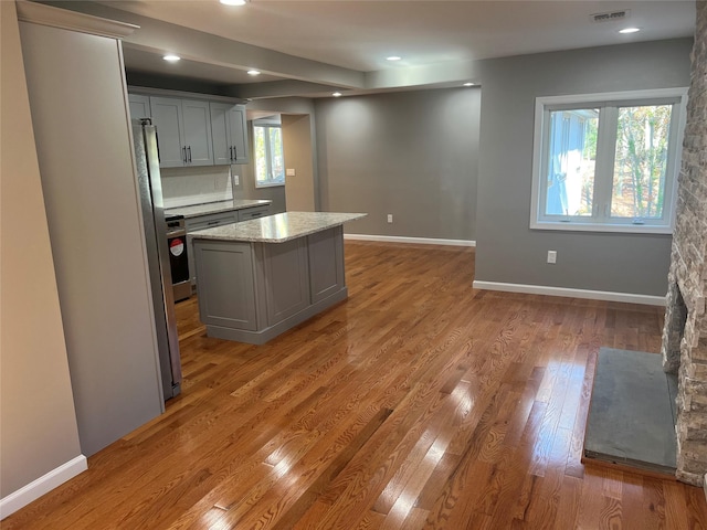 kitchen featuring light hardwood / wood-style floors, a center island, light stone countertops, and gray cabinetry