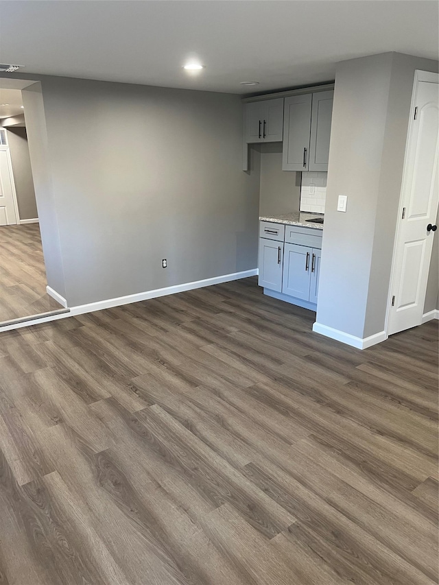 interior space with gray cabinets, decorative backsplash, light stone counters, and dark hardwood / wood-style floors