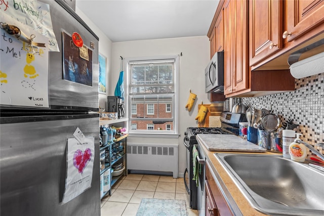 kitchen featuring light tile patterned floors, tasteful backsplash, radiator, appliances with stainless steel finishes, and a sink