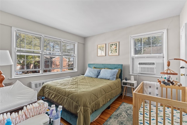 bedroom featuring multiple windows, radiator heating unit, and wood finished floors