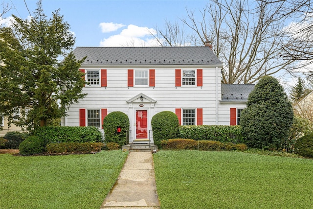 colonial-style house featuring a chimney, a high end roof, and a front yard