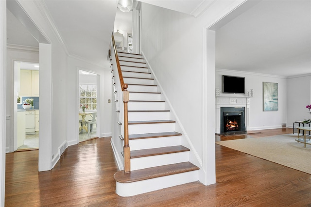 stairway featuring a lit fireplace, ornamental molding, and wood finished floors