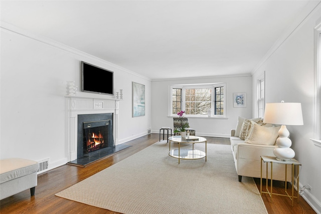 living room with a warm lit fireplace, wood finished floors, visible vents, and baseboards