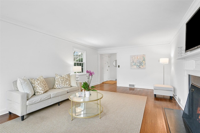 living area featuring baseboards, visible vents, a fireplace with flush hearth, ornamental molding, and wood finished floors