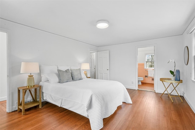 bedroom with ensuite bath, baseboards, and wood finished floors