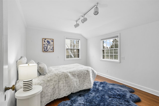 bedroom featuring lofted ceiling, rail lighting, baseboards, and wood finished floors