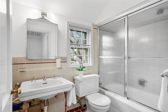 bathroom with enclosed tub / shower combo, a sink, tile walls, and toilet