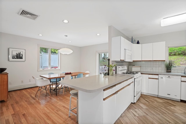 kitchen featuring white appliances, baseboard heating, a peninsula, healthy amount of natural light, and recessed lighting