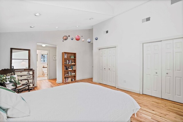 bedroom with multiple closets, high vaulted ceiling, light wood-style flooring, baseboards, and ensuite bathroom