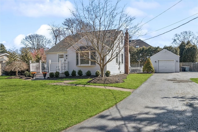 view of front facade with aphalt driveway, an outdoor structure, fence, a detached garage, and a front lawn