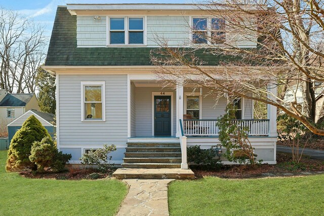 view of front facade with roof with shingles, a porch, and a front lawn