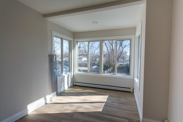 empty room with a baseboard heating unit, wood finished floors, and a wealth of natural light