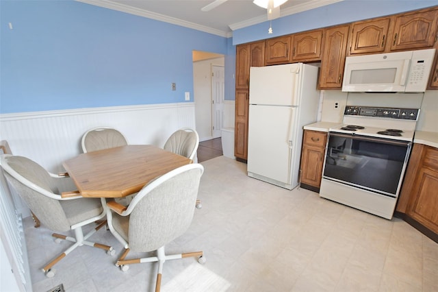 kitchen with brown cabinetry, white appliances, a wainscoted wall, and ornamental molding