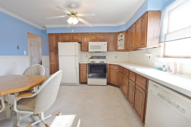 kitchen featuring brown cabinets, light countertops, wainscoting, a sink, and white appliances