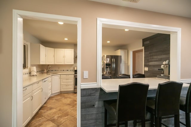 kitchen with white cabinets, light countertops, a kitchen bar, stainless steel refrigerator with ice dispenser, and a sink