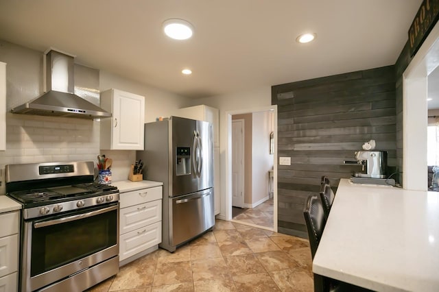 kitchen featuring light countertops, decorative backsplash, appliances with stainless steel finishes, white cabinets, and wall chimney exhaust hood