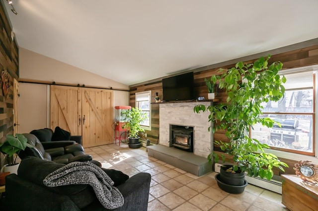 living area featuring lofted ceiling, a barn door, wooden walls, and a glass covered fireplace