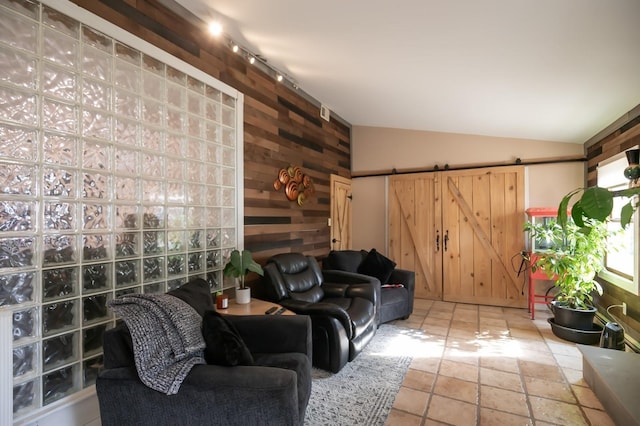 living room featuring vaulted ceiling, wooden walls, track lighting, and a barn door