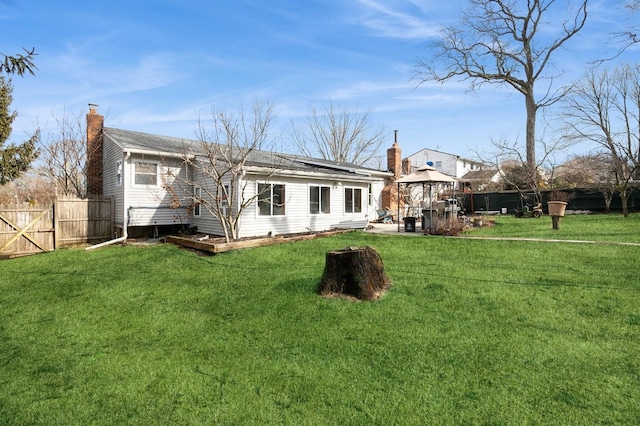 back of property with a gazebo, a chimney, fence, and a lawn