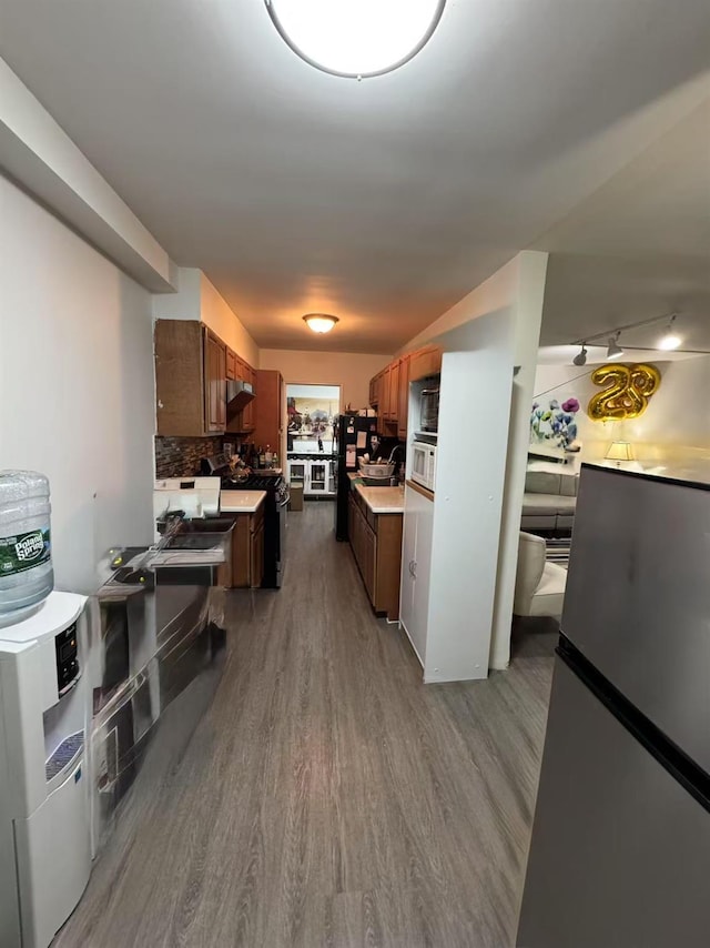 kitchen featuring light hardwood / wood-style flooring, washer / clothes dryer, black refrigerator, stainless steel refrigerator, and tasteful backsplash