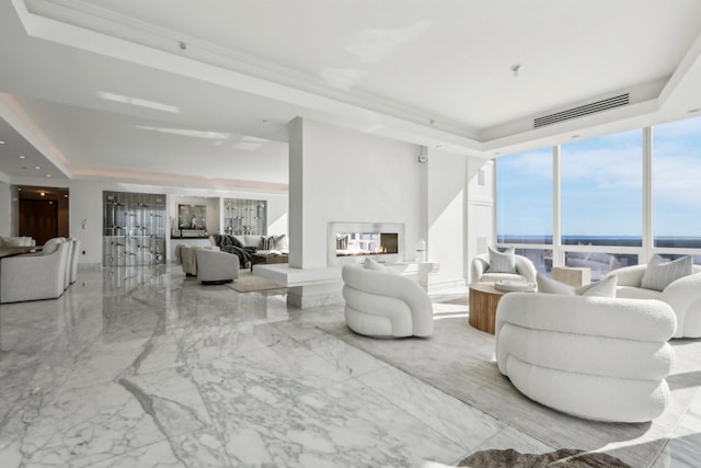 living area with a tray ceiling, marble finish floor, visible vents, and a glass covered fireplace