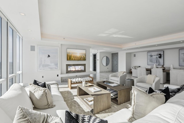 living room featuring a glass covered fireplace, a raised ceiling, and recessed lighting