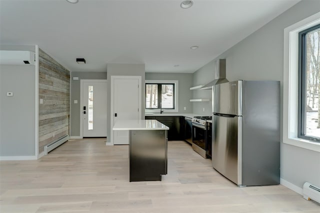 kitchen with appliances with stainless steel finishes, a kitchen island, wall chimney exhaust hood, and baseboard heating