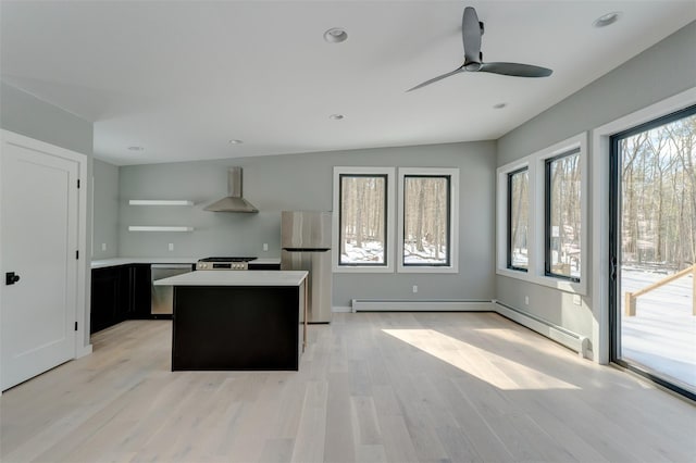 kitchen featuring a kitchen island, wall chimney range hood, light hardwood / wood-style floors, stainless steel appliances, and ceiling fan