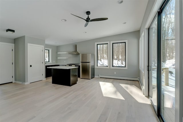 kitchen featuring light hardwood / wood-style flooring, appliances with stainless steel finishes, a kitchen island, wall chimney exhaust hood, and baseboard heating