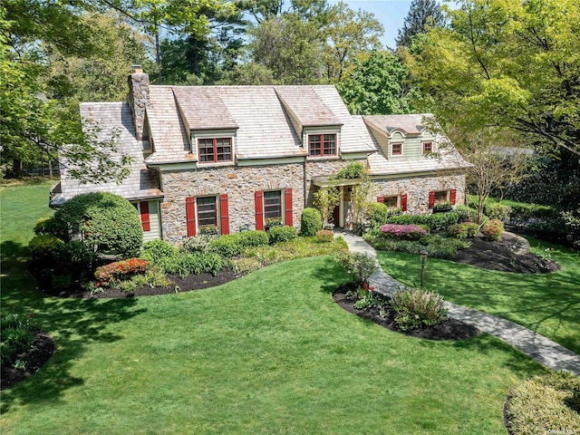 view of front of property with stone siding, a chimney, a high end roof, and a front yard