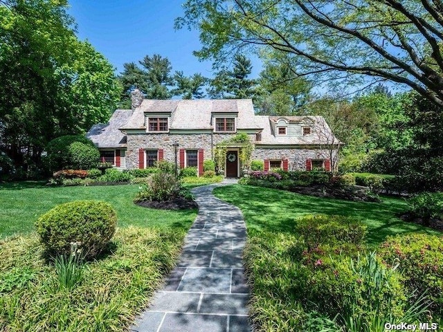 view of front facade featuring stone siding, a chimney, and a front lawn