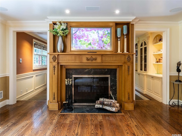 details featuring a wainscoted wall, a fireplace, wood finished floors, visible vents, and ornamental molding