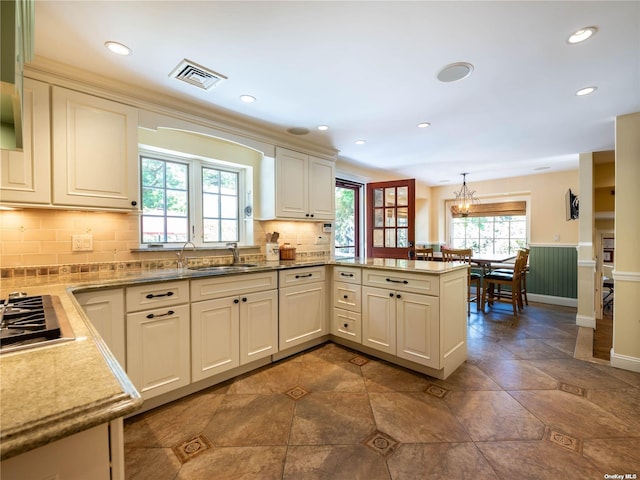 kitchen with visible vents, a peninsula, a sink, pendant lighting, and backsplash