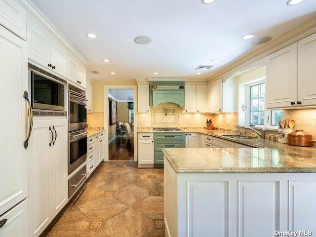 kitchen with a peninsula, a sink, white cabinets, appliances with stainless steel finishes, and tasteful backsplash