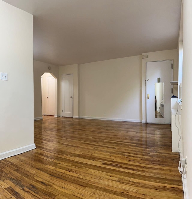 spare room with baseboards, arched walkways, and dark wood finished floors