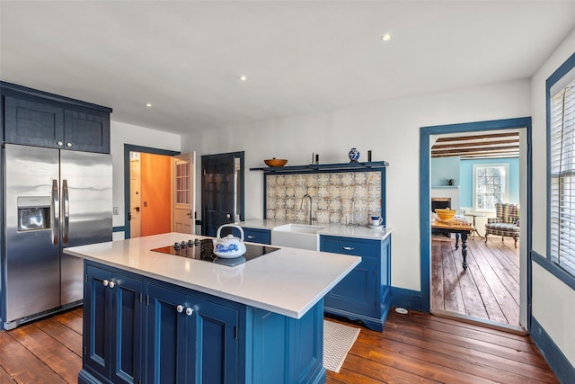 kitchen featuring an island with sink, black electric stovetop, stainless steel refrigerator with ice dispenser, blue cabinets, and sink