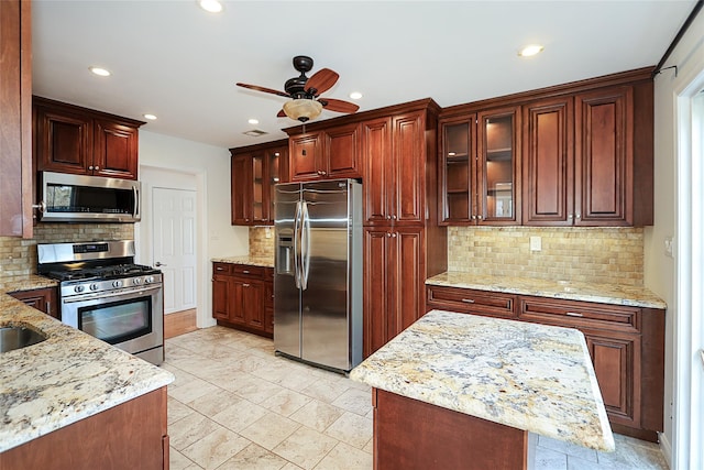 kitchen with glass insert cabinets, light stone counters, a ceiling fan, and appliances with stainless steel finishes