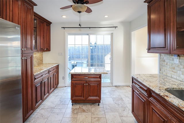 kitchen with light stone countertops, a ceiling fan, backsplash, and stainless steel refrigerator