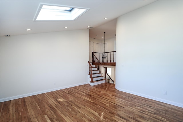 spare room with wood finished floors, recessed lighting, a skylight, baseboards, and a towering ceiling