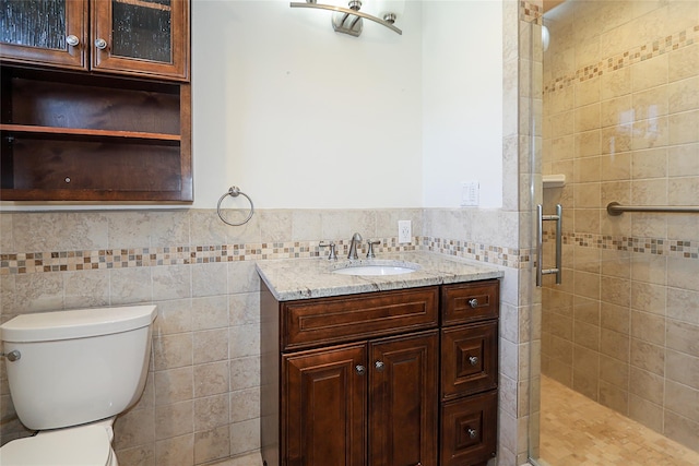 bathroom with a shower stall, toilet, vanity, wainscoting, and tile walls