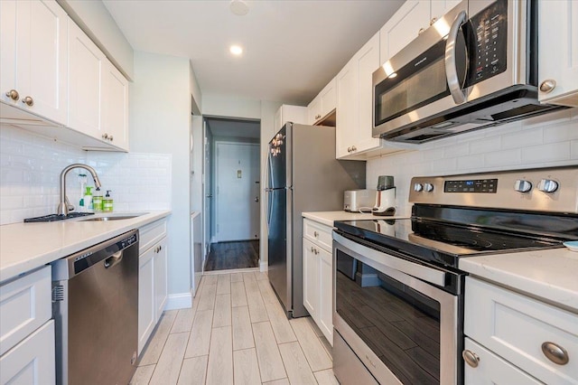 kitchen with wood finish floors, a sink, white cabinetry, light countertops, and appliances with stainless steel finishes