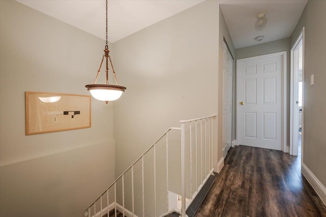 hallway with dark wood-style flooring, baseboards, and an upstairs landing