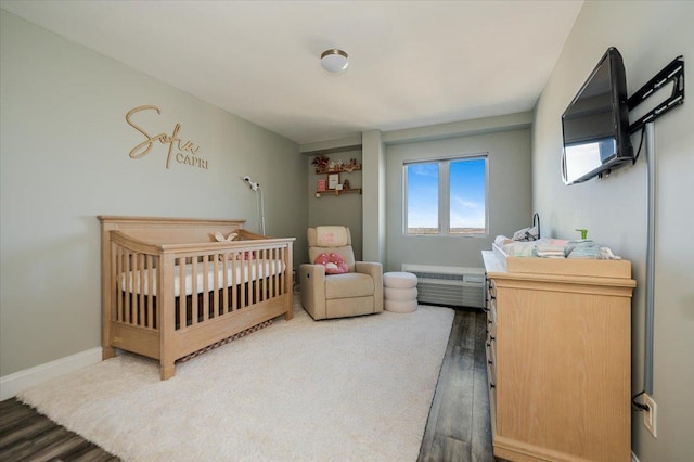 bedroom with a crib, a wall mounted air conditioner, wood finished floors, and baseboards