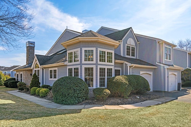 view of front of home with driveway, a chimney, an attached garage, and a front yard