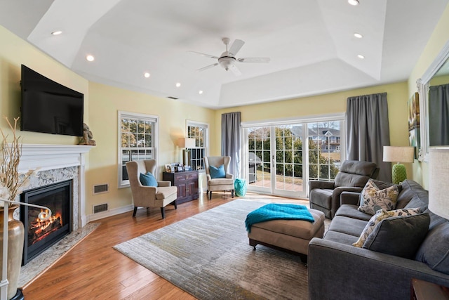 living area with a tray ceiling, recessed lighting, visible vents, a high end fireplace, and wood finished floors