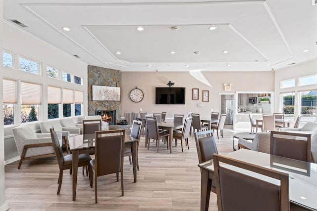 dining area with a tray ceiling, visible vents, a fireplace, and light wood finished floors