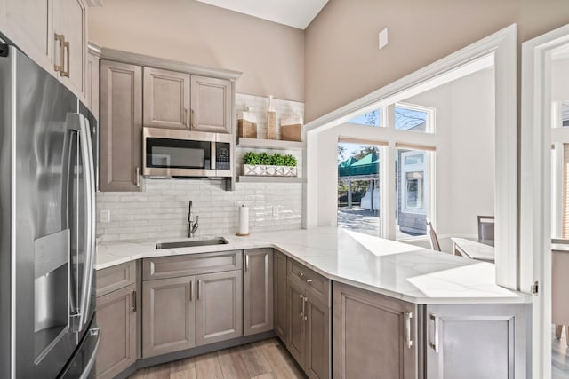 kitchen with stainless steel appliances, a peninsula, a sink, backsplash, and open shelves