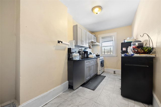 kitchen with dark countertops, gray cabinets, white range with gas stovetop, under cabinet range hood, and baseboards