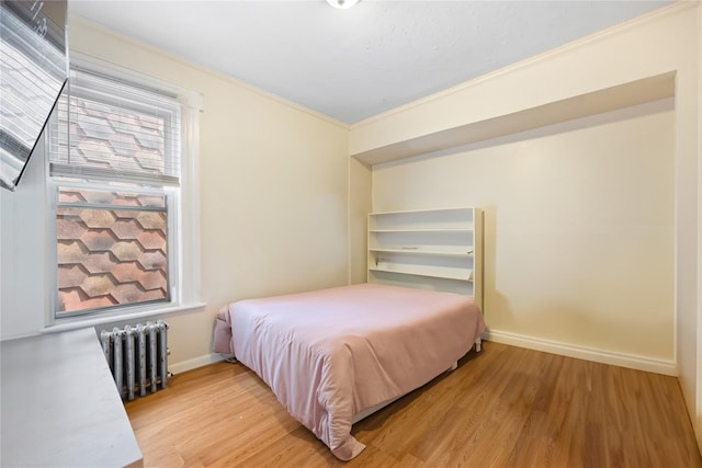 bedroom with light wood finished floors, radiator heating unit, baseboards, and crown molding