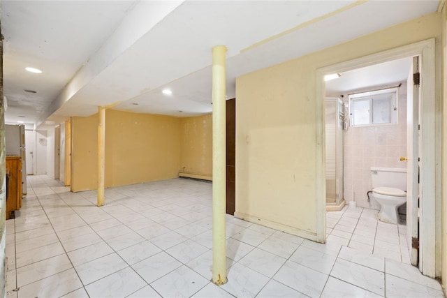 basement featuring freestanding refrigerator, recessed lighting, baseboard heating, and light tile patterned floors